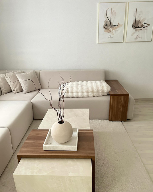 Beżowa sofa z drewnianymi nóżkami i niebieskimi poduszkami akcentującymi wnętrze.