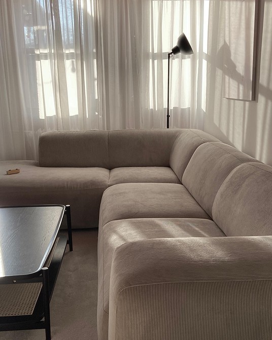 Nowoczesna beżowa sofa na drewnianych nóżkach na tle jasnej ściany