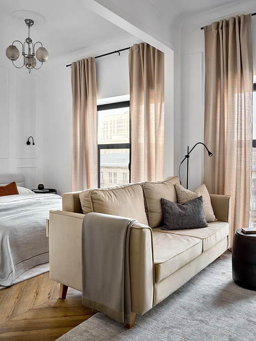 Narożna beżowa sofa z poduszkami w różnych odcieniach w jasnym pokoju.