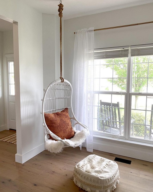 Relaks w kokonie Fotel wiszący kokon w jasnym wnętrzu, idealny kącik relaksu przy oknie.