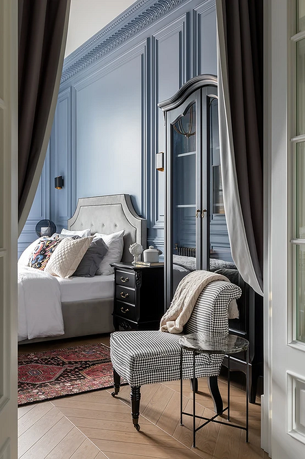 Stylowa sypialnia z dużym szarym łóżkiem, dekoracyjnymi poduszkami i szafkami nocnymi.