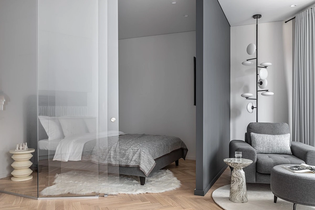 Nowoczesna sypialnia z szarym łóżkiem i minimalistycznym dekorem na ścianie.