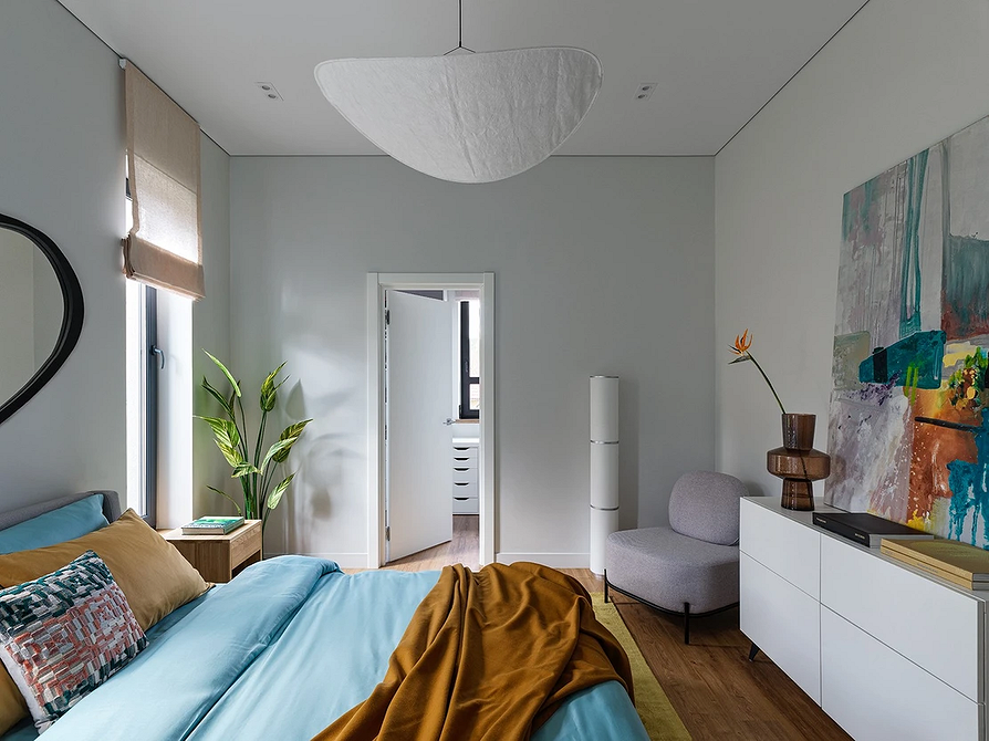 Nowoczesna sypialnia z szarym łóżkiem, minimalistycznymi szafkami nocnymi i dekoracyjnymi poduszkami.