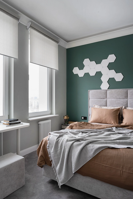 Szare łóżko w sypialni, dywan i elementy dekoracyjne utrzymane w tonacji.