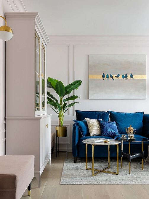 Niebieska sofa w nowoczesnym salonie z kolorowymi poduszkami i jasnymi akcentami.