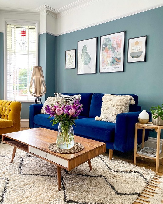 Przytulny salon z niebieską sofą, pledem i dekoracyjnymi poduszkami na дивані.