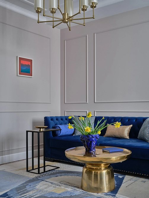 Salon z narożną, niebieską sofą, drewnianym stolikiem i zielonymi roślinami.