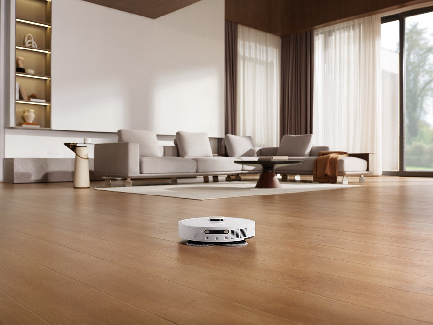 Dom lśni czystością. Estetyczny robot sprzątający autonomicznie pracuje na jasnym tle.